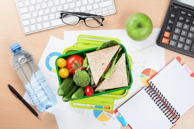 Person working at a desk with a notebook, water bottle, and a small bowl of mixed nuts and fruit for an afternoon break